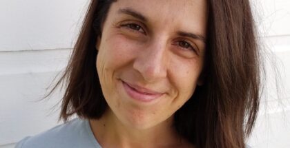 Image shows a woman in a greyish top smiling at the camera
