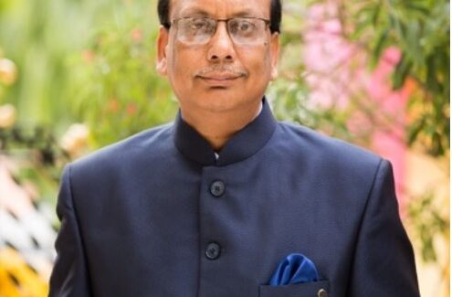 Image shows a balding Indian man wearing a dark coloured shirt looking at the camera